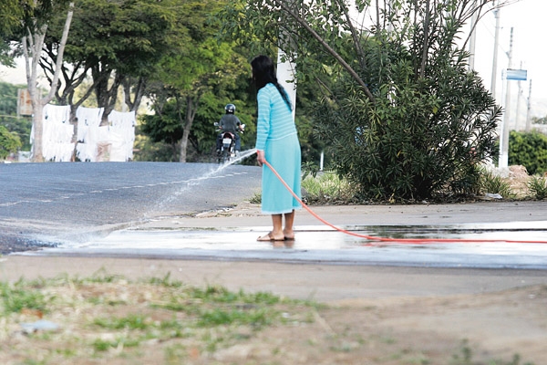 Mulher lava calçada com mangueira. Nesta época de seca, tal ato é uma falta de cidadania 